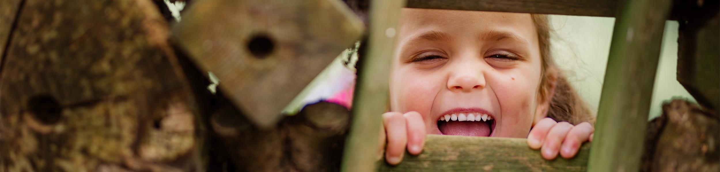 smiling child looks through gap in fence