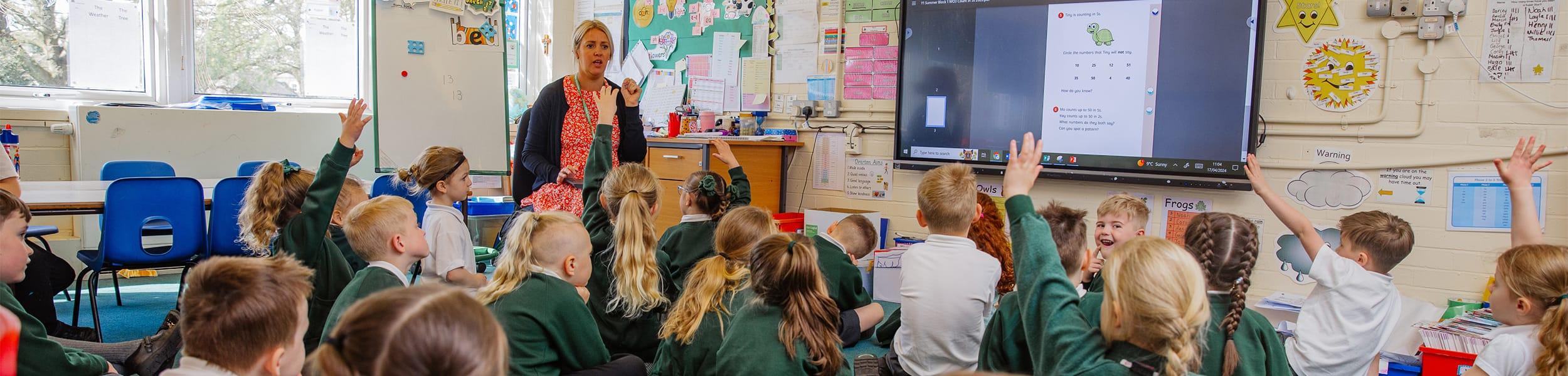 teacher and class of children with hands up